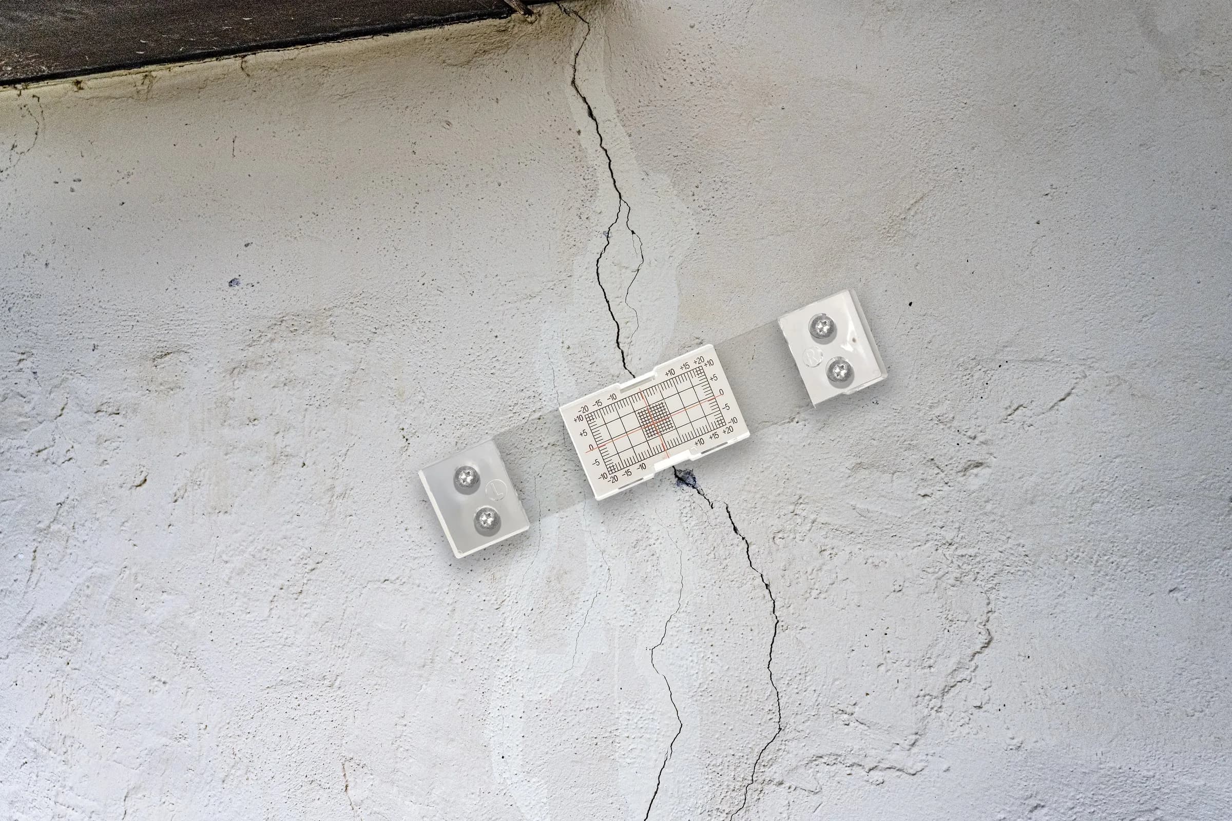 Risssiegel mit Messraster über einem Riss in einer verputzten Fassade