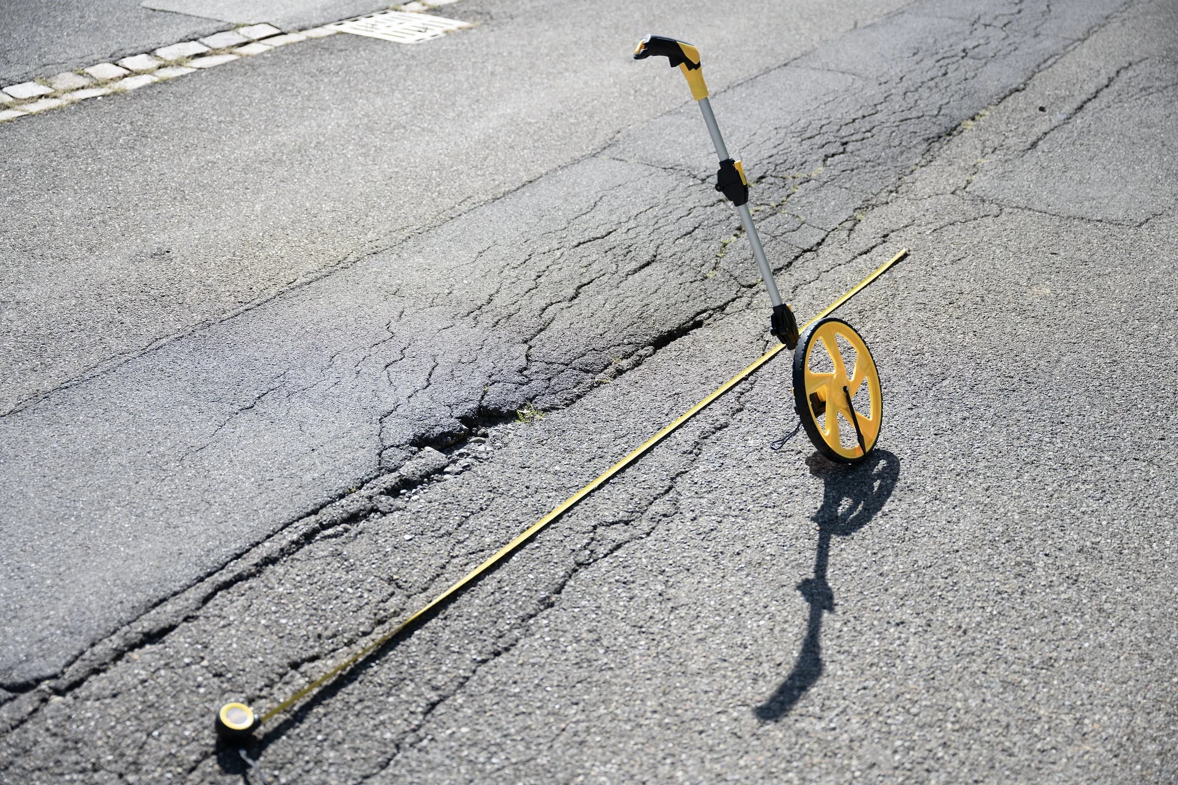 Messrad und Massband auf einem aufgerissenen Strassenbelag