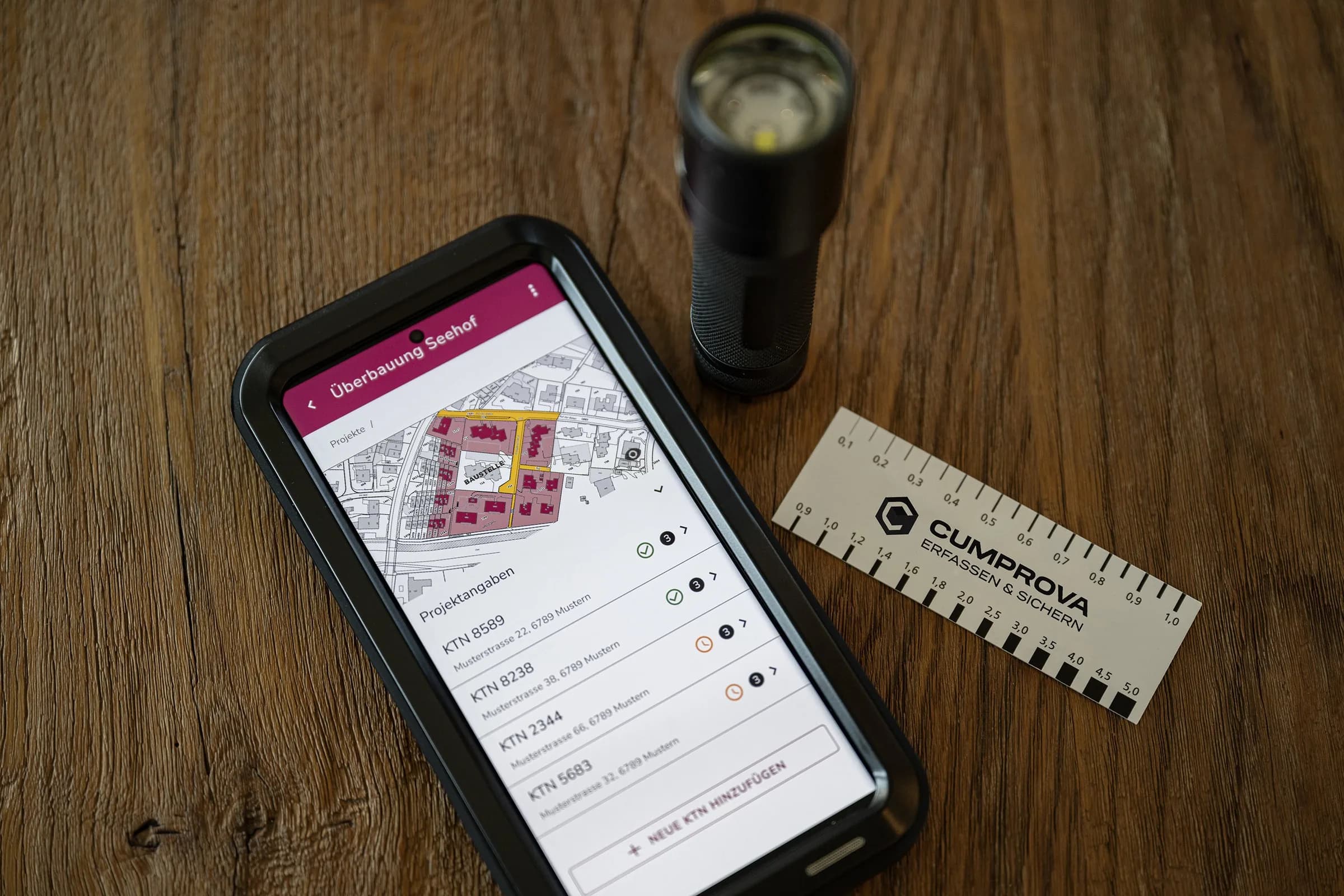 Die Cumprova App auf dem Smartphone, daneben Prüflampe und Messlineal